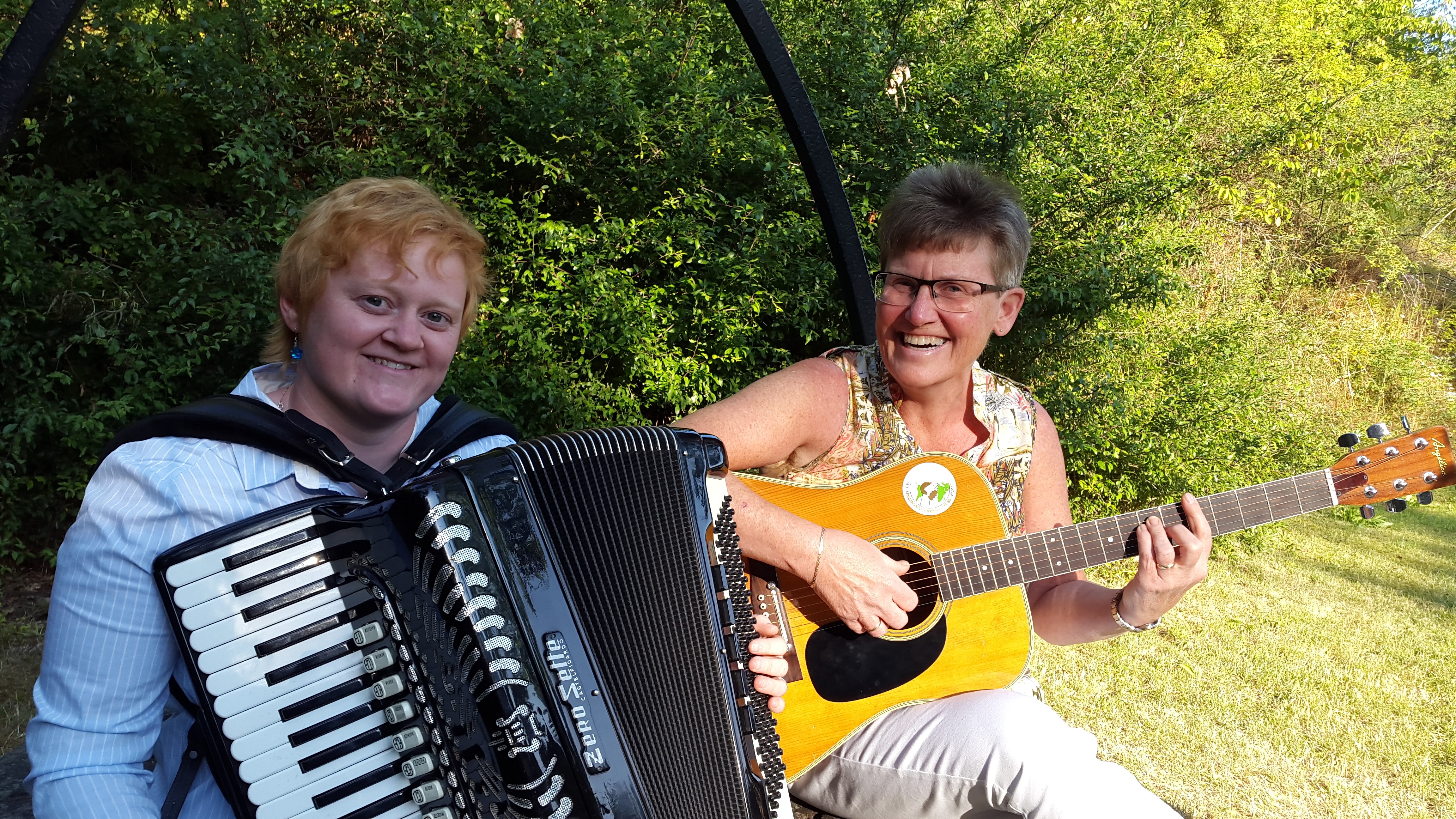 MArianne med trekkspill og Anne Karine med gitaren sittende på brønnen ved Løvøykapellet